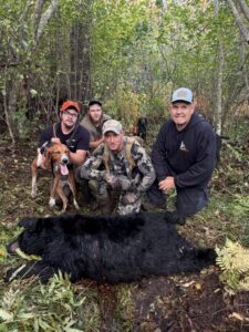 Hunting party posing with a black bear and their hounds