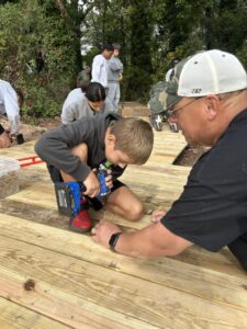 A volunteer helps a young builder fasten decking